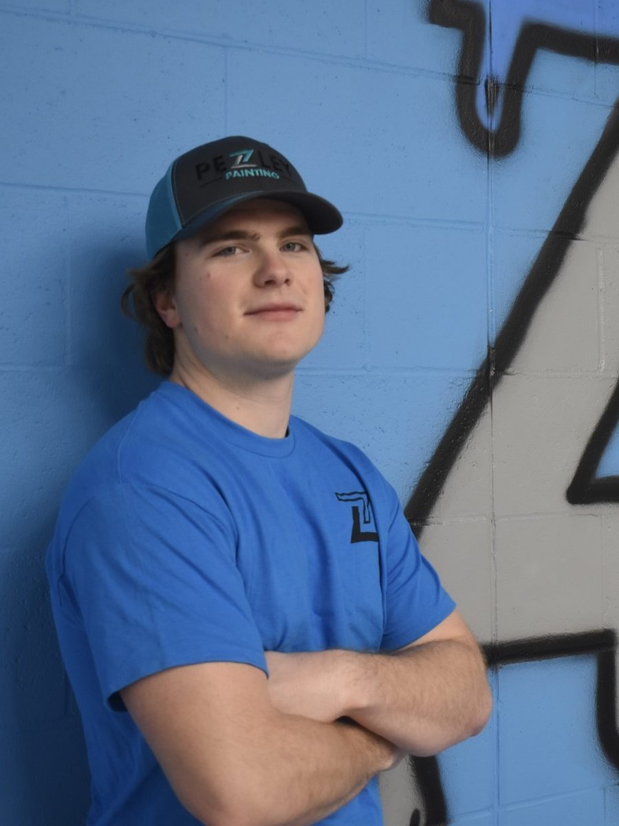 Pezley Painting team member standing by the brand logo wall