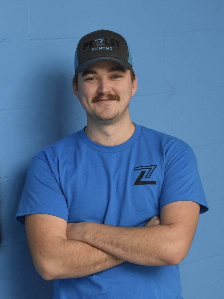 Pezley Painting team member smiling in front of the logo mural