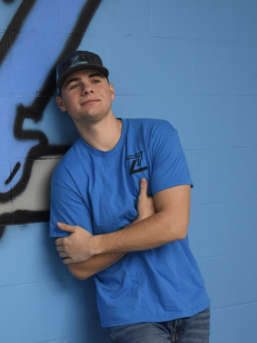 Pezley Painting team member leaning against the blue brand wall
