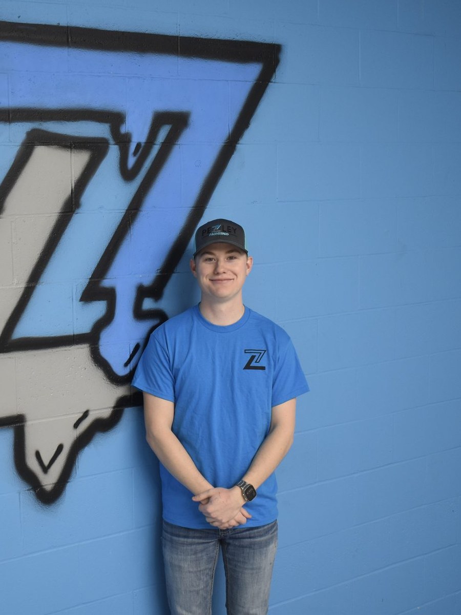 Pezley Painting team member standing beside the logo mural