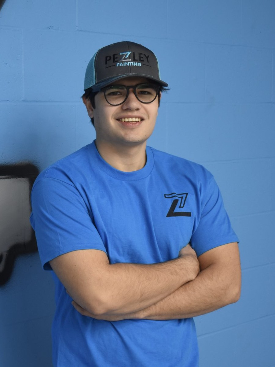 Pezley Painting team member with arms crossed by the logo wall